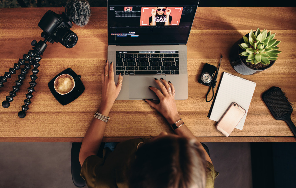 A female editing a video she shot using her laptop at home. With camera and tripod on the table