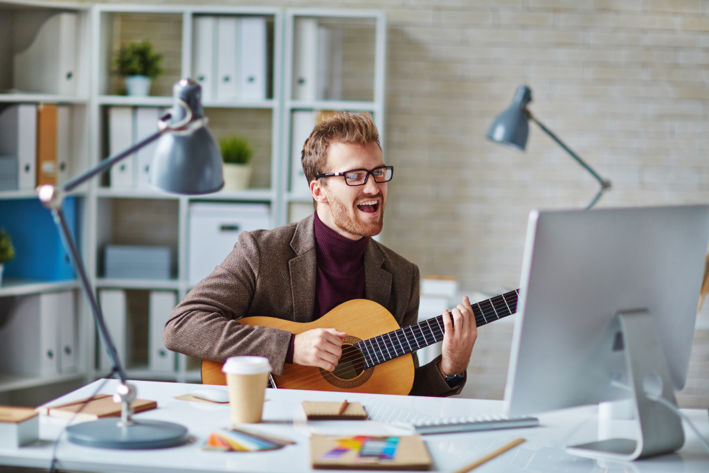 A handsome man singing and playing the guitar while recording in front of the computer