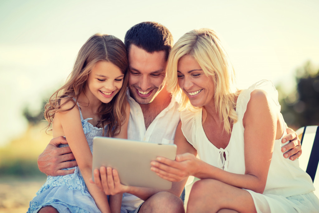 a child, together with her parents, watches something in their Ipad.